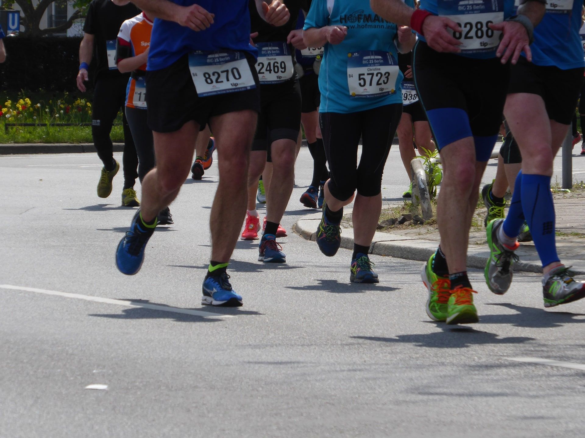 Teilnehmende an einem Marathon. In der Aufnahme sind die Gesichter abgeschnitten. Die Teilnehmer joggen auf der Straße, im Hintergrund ist ein Beet mit Frühlingsblühern.