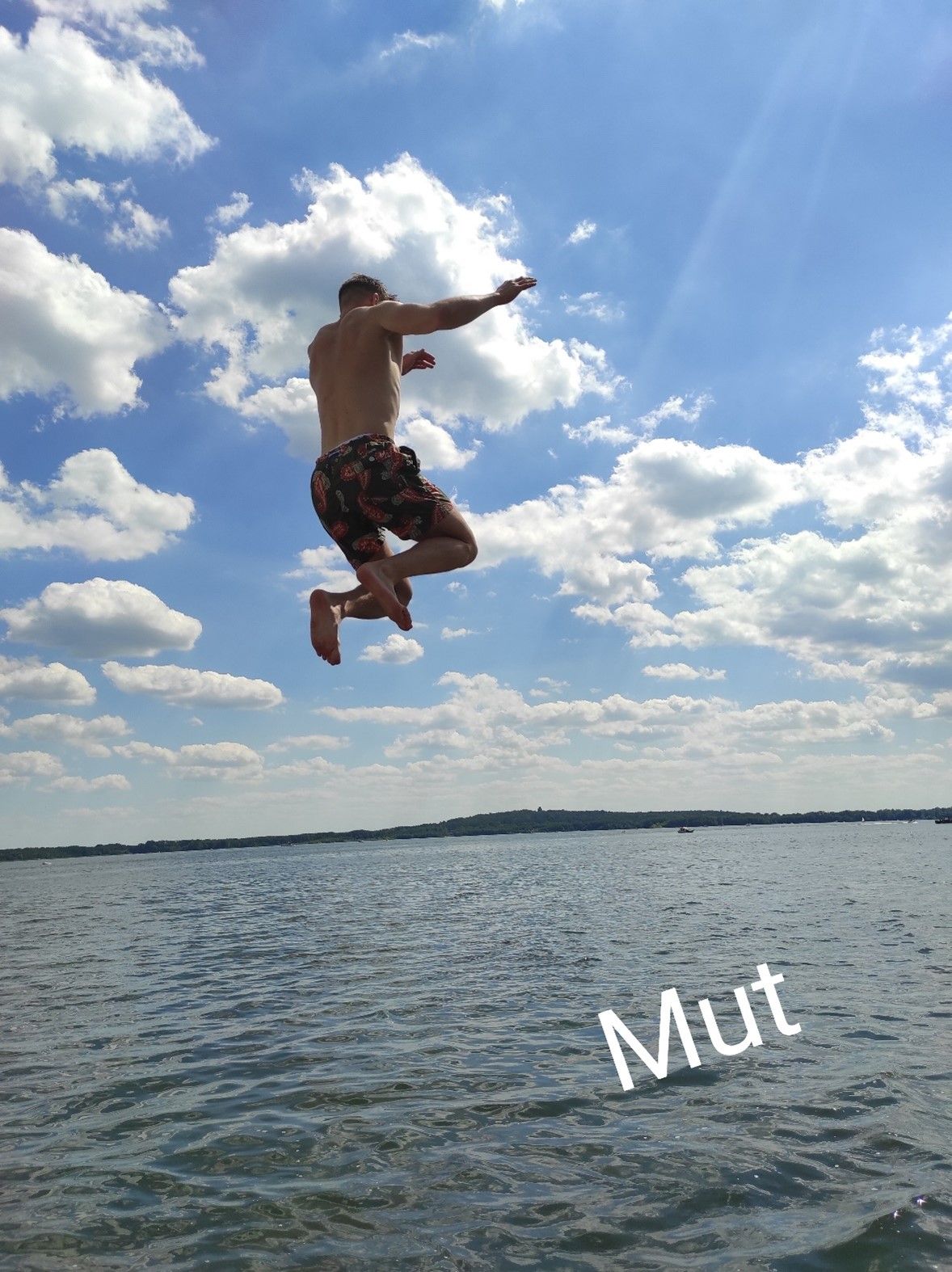 Mann springt mutig ins Wasser unter einem blauen Himmel mit Wolken, mit dem Wort 'Mut' im Bild.
