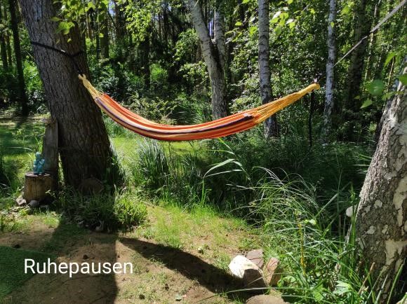 Hängematte zwischen Bäumen in einem grünen Garten mit dem Wort 'Ruhepausen.'