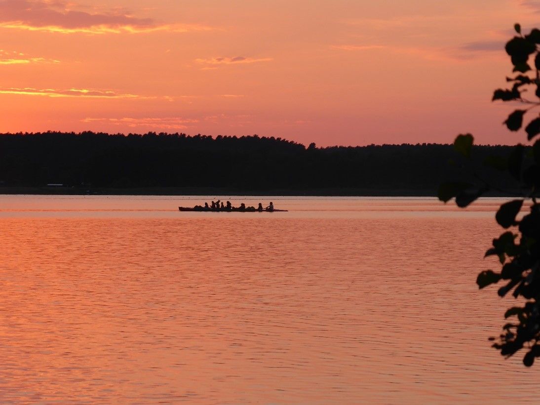 Kanufahrer auf einem See bei Sonnenuntergang, das Wasser leuchtet in warmen Orange- und Rottönen
