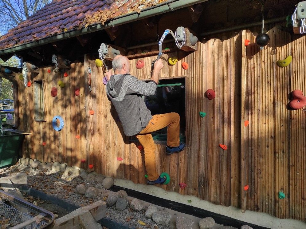 Mann klettert an einer Holzwand mit Klettergriffen und nutzt Eisgeräte für den Aufstieg